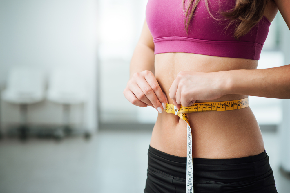 A view of a tummy of a woman wrapped around a measuring tape with depth of field on the background