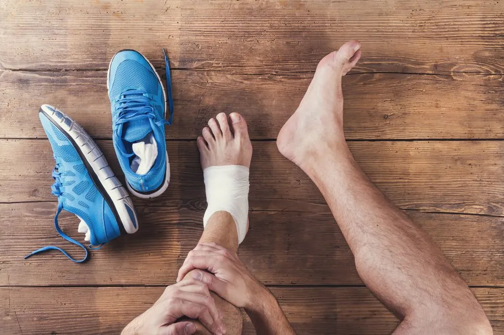 Top shot of a 2 pair of feet with a bandage on the left foot and blue shoes lying around
